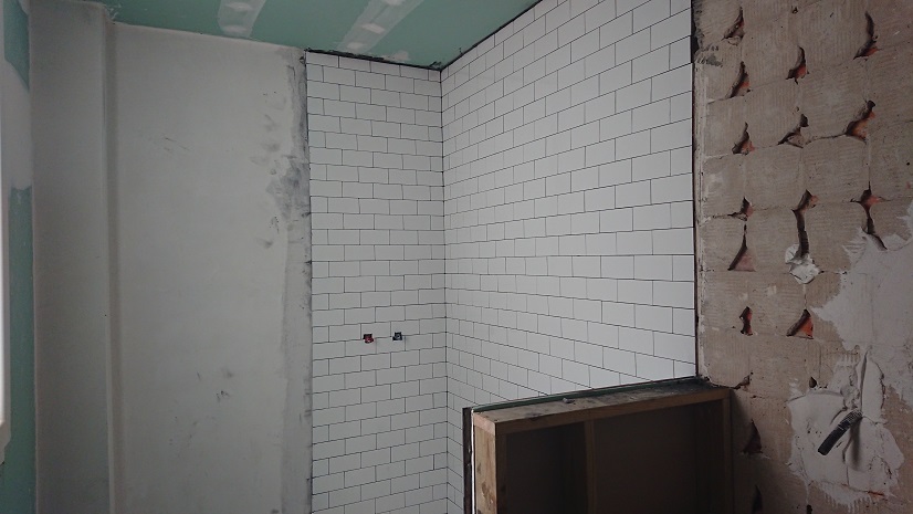 Zona de ducha con azulejos blancos lisos y suelo gris durante la obra.